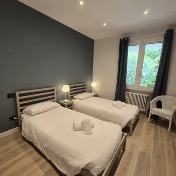 Two single beds in a cozy bedroom with a chair and window.