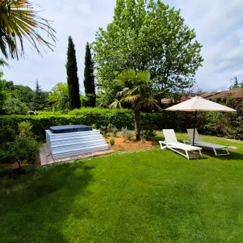 Lush garden with sunbeds, umbrella, and a pool under a partly cloudy sky.