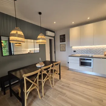 Dining area and modern kitchen with wooden chairs and pendant lights.
