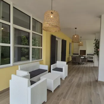 Covered patio with white chairs and a wooden floor, set against yellow walls.