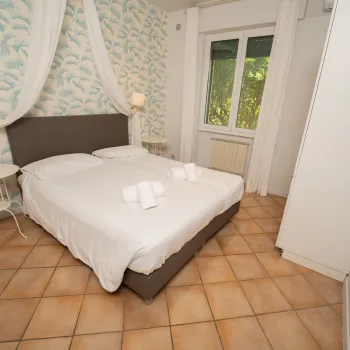 Cozy bedroom with a double bed, white curtains, and patterned wallpaper.