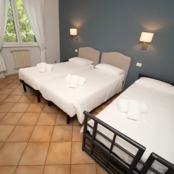 Three neatly made beds in a bright room with tiled floor and wall lamps.