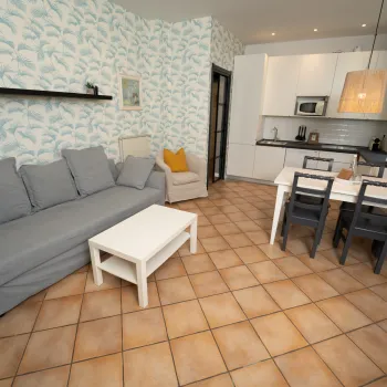 Living room with gray sofa, white table, dining set, and kitchen in background.