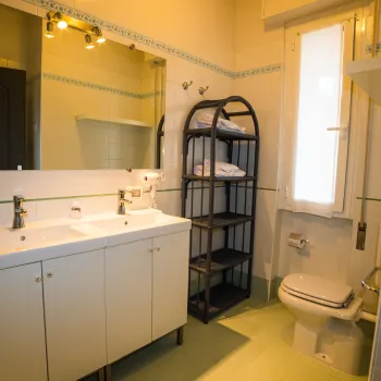 Bright bathroom with double sink, towel rack, and toilet.