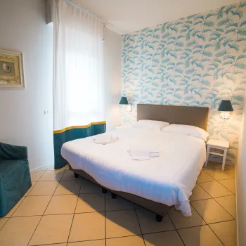 Cozy bedroom with a double bed, teal armchair, and patterned wallpaper.