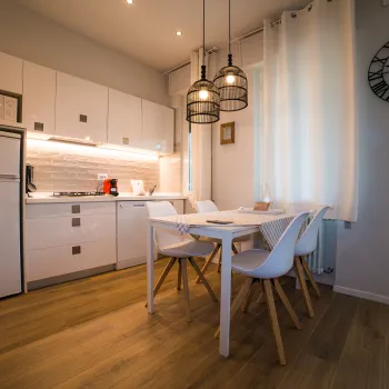 Modern kitchen and dining area with white cabinets, wooden floor, and large wall clock.