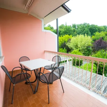 Balcony with pink walls, four chairs, and a table overlooking greenery.
