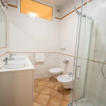 Modern bathroom with shower, sink, toilet, and bidet; light tile and glass details.