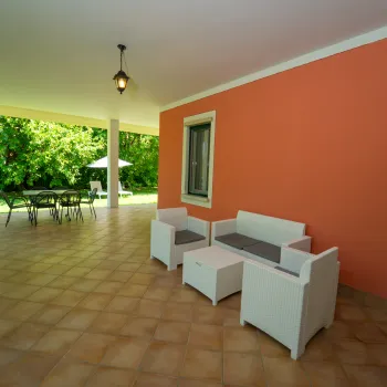 Covered patio with orange wall, white furniture, and garden view.
