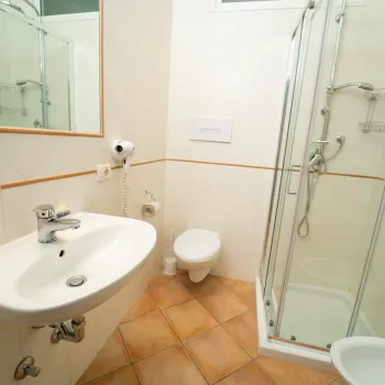 Small bathroom with sink, toilet, and glass shower enclosure. White tiles and mirror.