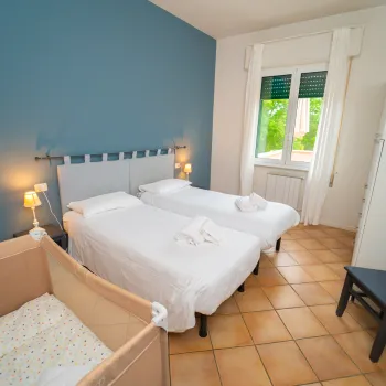 Two single beds, a crib, and a chair in a sunlit room with blue and white walls.