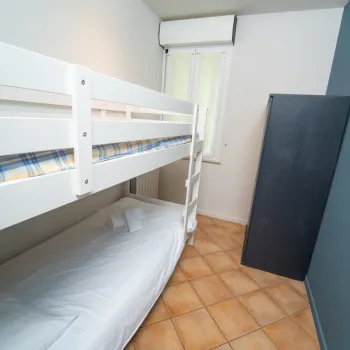 White bunk bed in a small room with tiled floor, blue wall, and a window.
