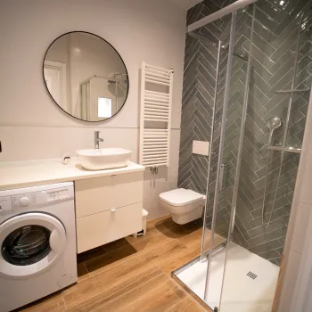 Modern bathroom with a shower, washing machine, and round mirror.