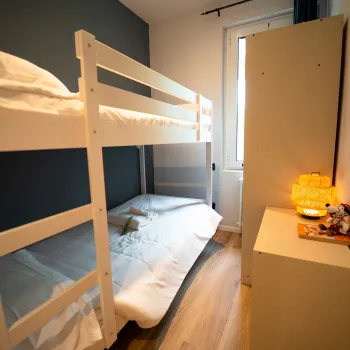 Small bedroom with a white bunk bed, soft lighting, and a narrow window.