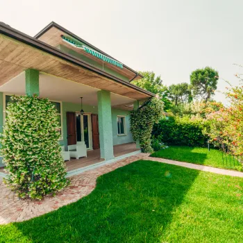 Modern house with a lush green lawn and trees on a sunny day.