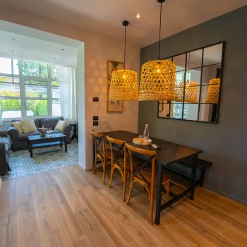Dining area with wooden table, wicker chairs, pendant lights, and adjacent cozy living room.