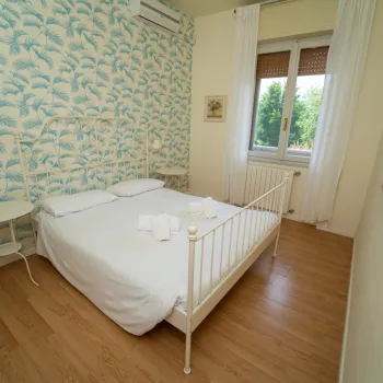 Bright bedroom with a double bed, floral wallpaper, and a window with curtains.