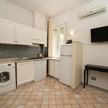 Compact kitchen with washing machine, fridge, TV, and black table.