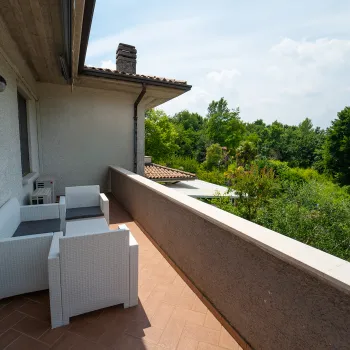 Balcony with white chairs overlooking lush green trees.