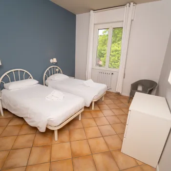 Twin beds in a bright room with tiled floor and window overlooking greenery.