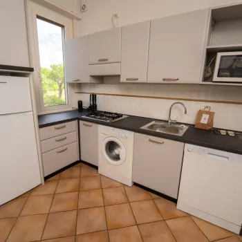 Compact kitchen with white cabinets, washing machine, microwave, and fridge.