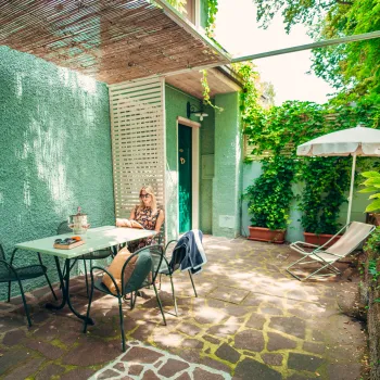 Cozy patio with green walls, a small table, chairs, and plants in sunlight.