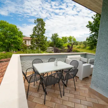 Terrace with table, chairs, and sofa under a blue sky with trees in the background.