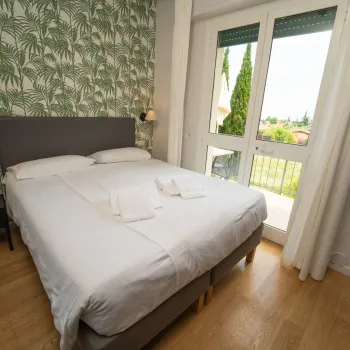 Cozy bedroom with a double bed, palm print wallpaper, and garden view.
