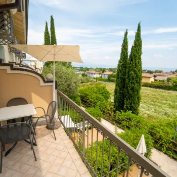 Balcony with table, chairs, view of trees and fields under a blue sky.