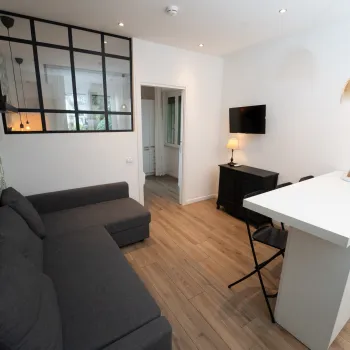 Modern living room with gray sofa, wall-mounted TV, and pendant lights over a white counter.