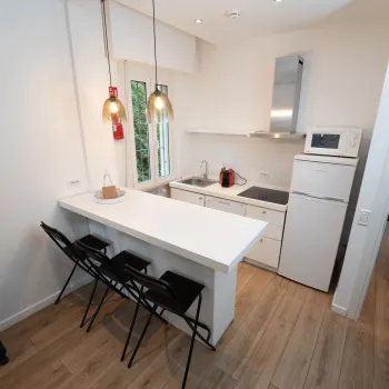 Small kitchen with white counters, bar stools, and hanging lights.