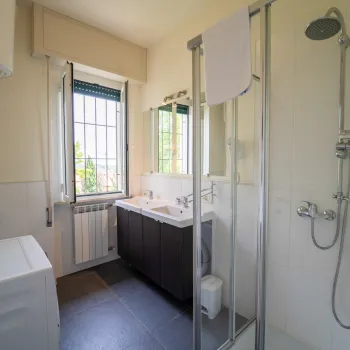 Bright bathroom with shower, washer, and vanity under a window.