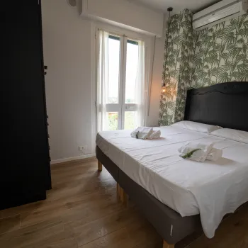 Cozy bedroom with large bed, leafy wallpaper, and natural light from a window.