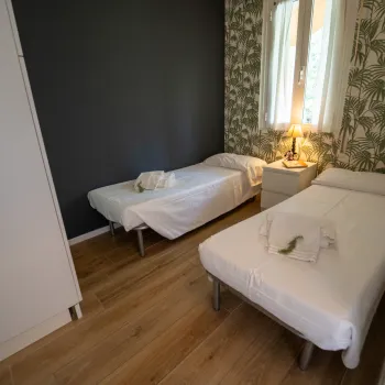 Two single beds in a cozy, plant-themed room with a nightstand and lamp between them.