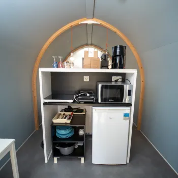 Compact kitchenette with fridge, microwave, and coffee maker in an arched room.