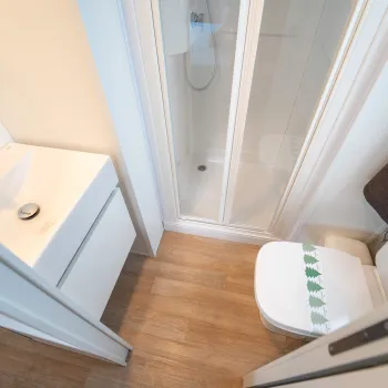 Compact bathroom with shower, toilet, sink, and wood flooring.