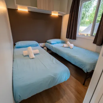 Two single beds with blue sheets in a small, bright room.