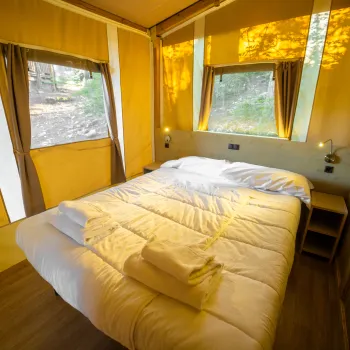 Cozy cabin bedroom with a large bed, natural light, and forest view through windows.