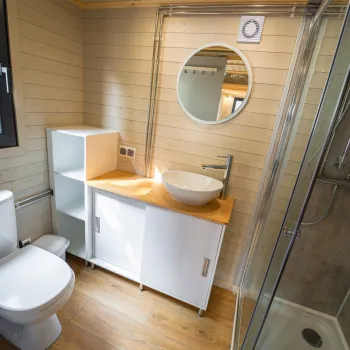 Small modern bathroom with wood accents, round mirror, and glass shower.