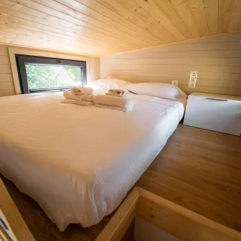 Cozy loft bedroom with white bed, wooden walls, and windows.