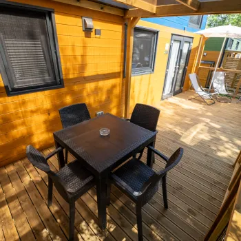 Wooden deck with table, chairs, and umbrella beside a yellow building.