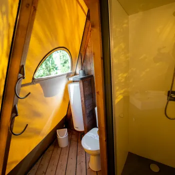 Bathroom with yellow light, shower, toilet, and wooden floor.