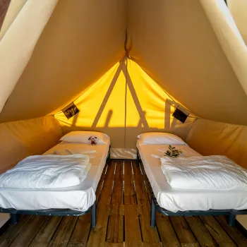 Cozy glamping tent interior with two single beds and warm lighting.