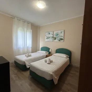 Two neatly made single beds in a small, bright room with wall art.