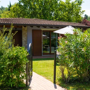 Small house with wooden doors, surrounded by greenery and trees.