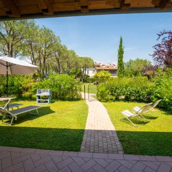 Sunny garden with chairs, umbrellas, and a path leading to lush greenery.