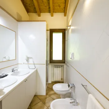Modern bathroom with two sinks, a bidet, and a window.