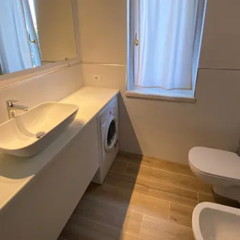 Modern bathroom with sink, mirror, and toilet; wooden floor; herringbone tiles.