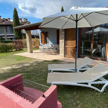 Patio with sun loungers, umbrella, and a red brick barbecue in a garden setting.