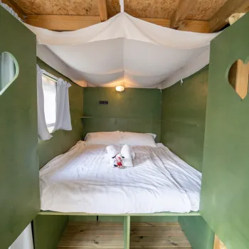 Cozy green cabin bed with heart-shaped cutouts, white sheets, and towel swans.